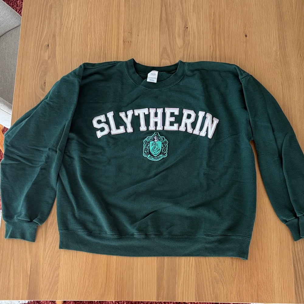Large crewneck sweatshirt that says Slytherin with the house emblem, worn